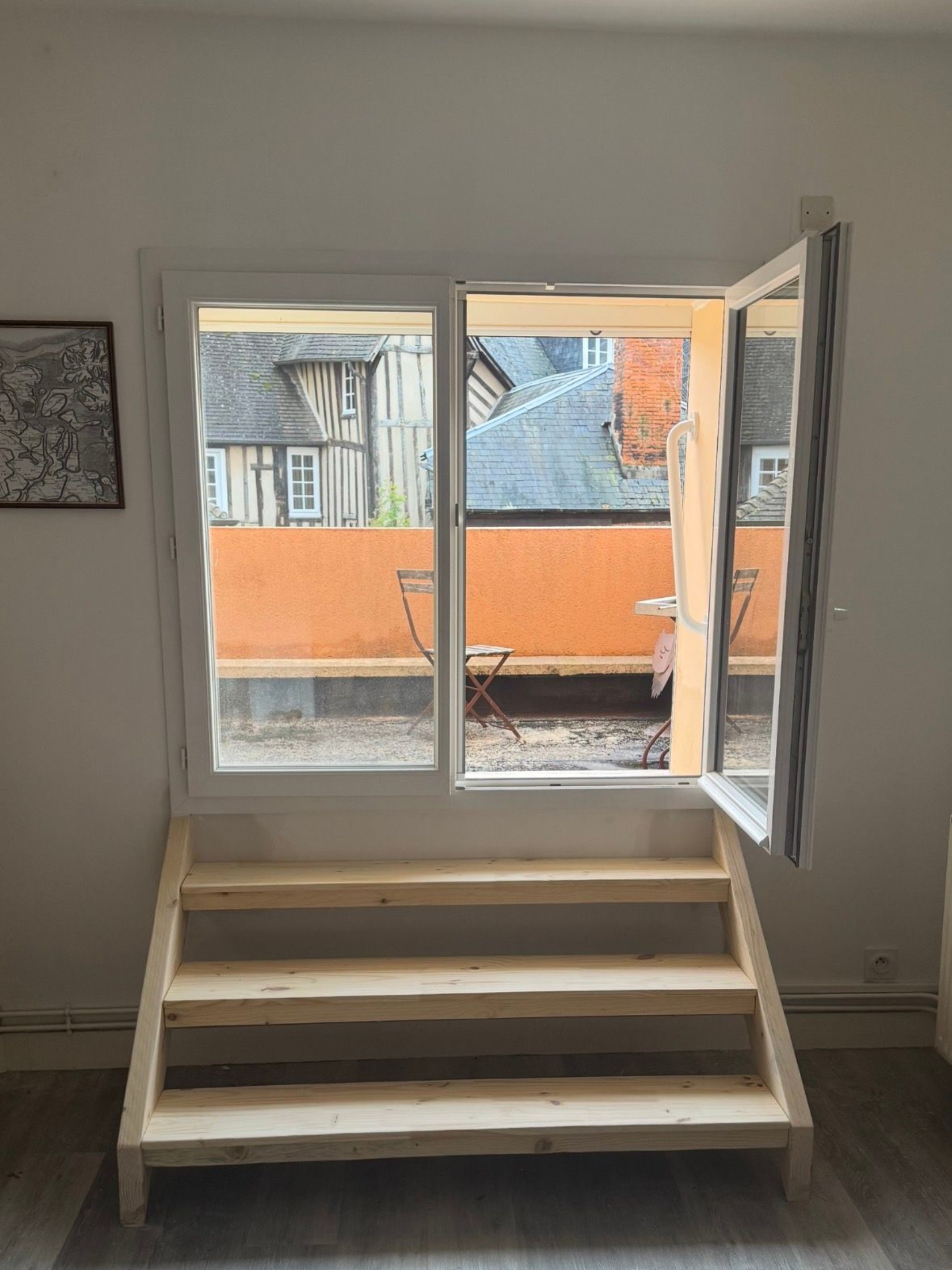 Petit escalier intérieur menant à une fenêtre ouverte et à un balcon aux murs extérieurs orange.