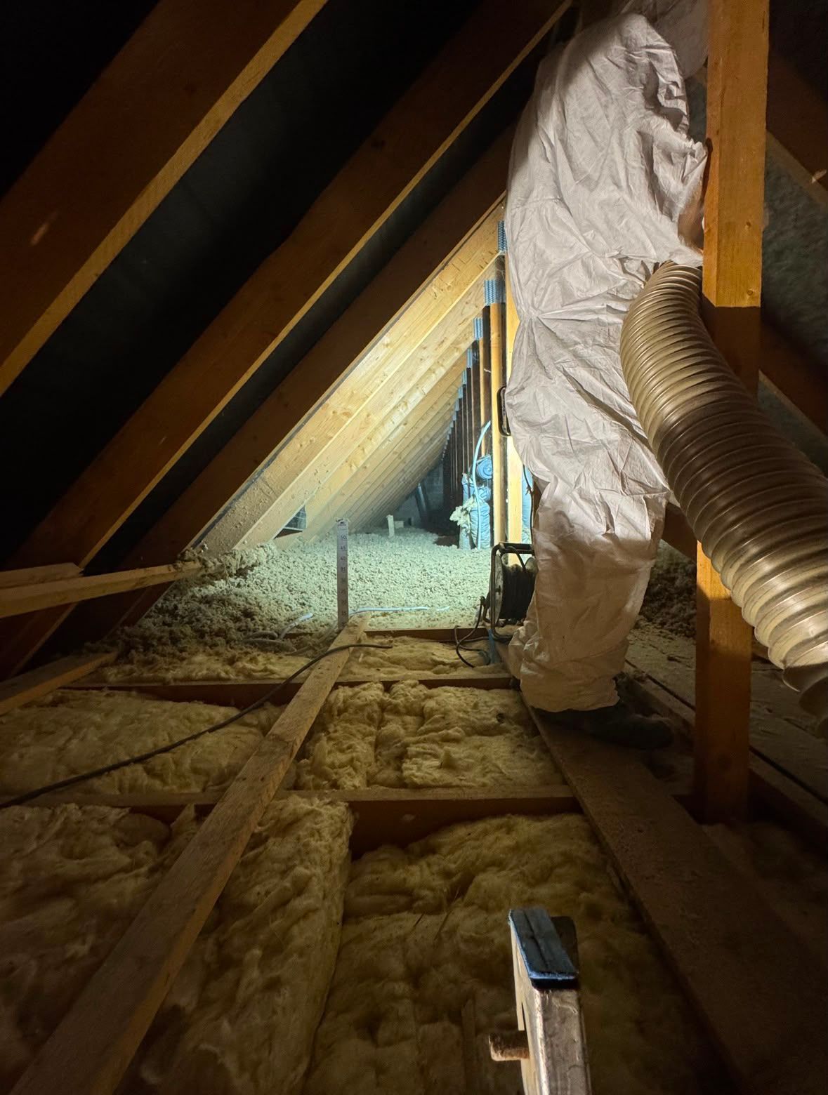 Intérieur du grenier avec isolation, poutres en bois et tuyau ondulé.