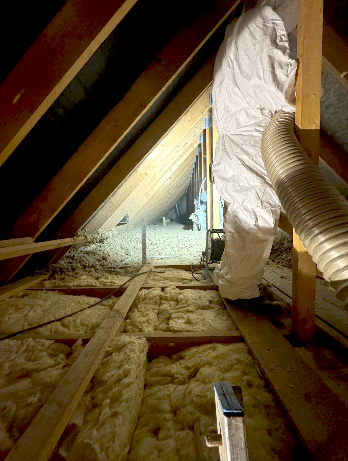 Grenier isolé, poutres en bois, mur en briques et tuyau d'aspirateur, éclairé par une lampe de travail.