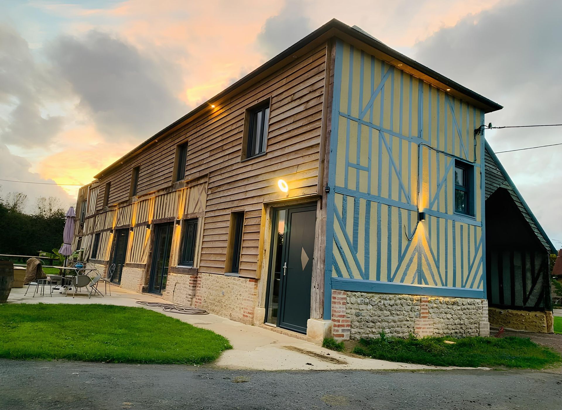 Bâtiment rustique de style grange au coucher du soleil, avec bardage en bois, base en pierre et accents de peinture/garniture bleue.