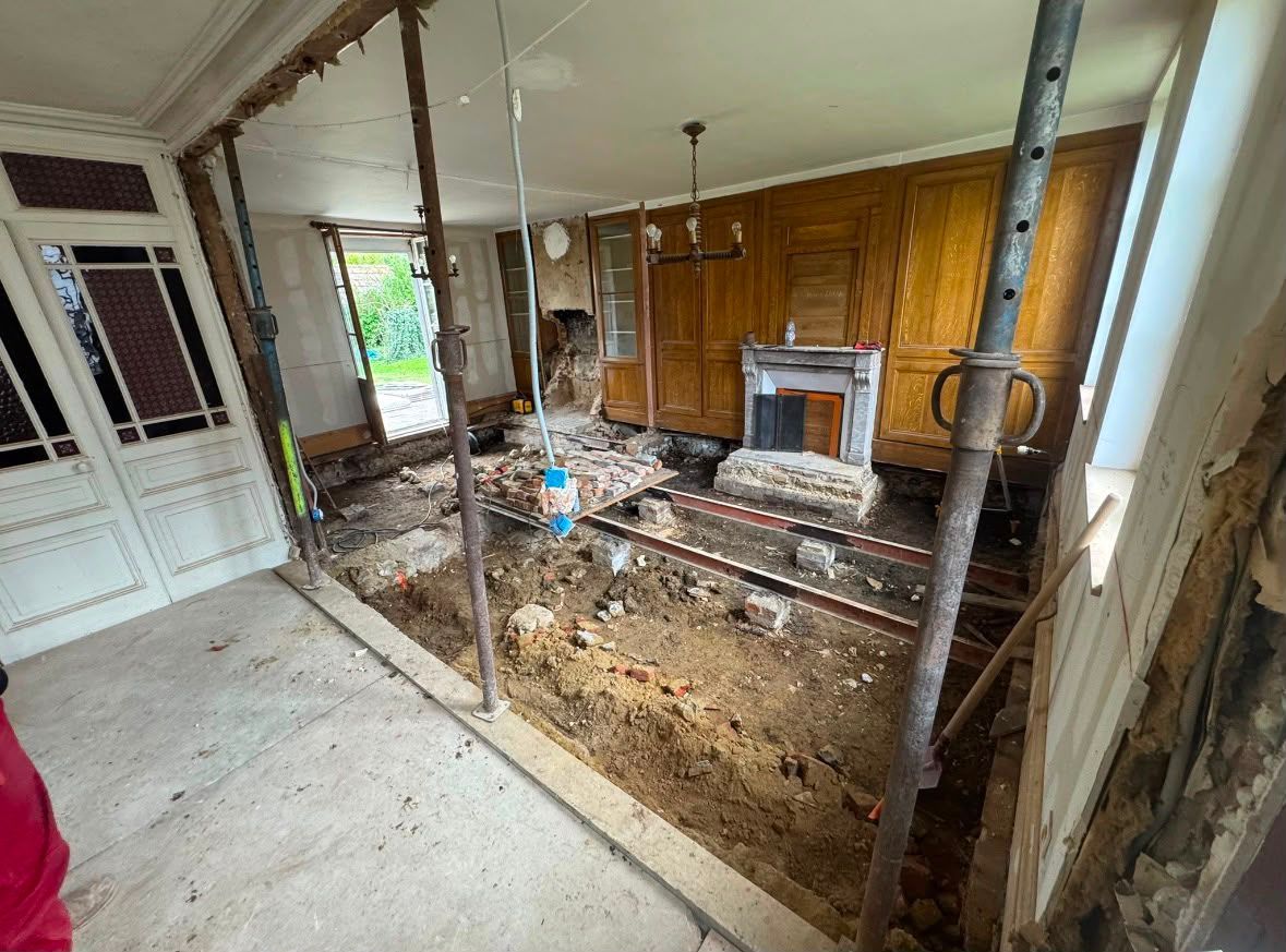 Salon endommagé avec solives apparentes, débris et cheminée en cours de rénovation