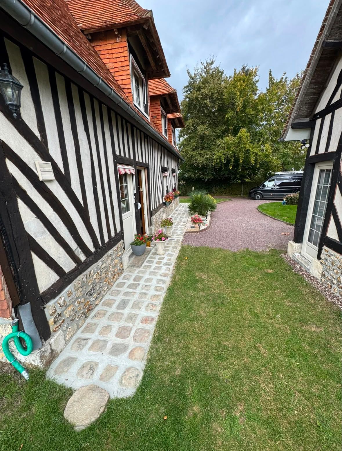Extérieur d'une maison à colombages avec un chemin de pierre, une pelouse verte, des pots de fleurs et une voiture garée dans la cour