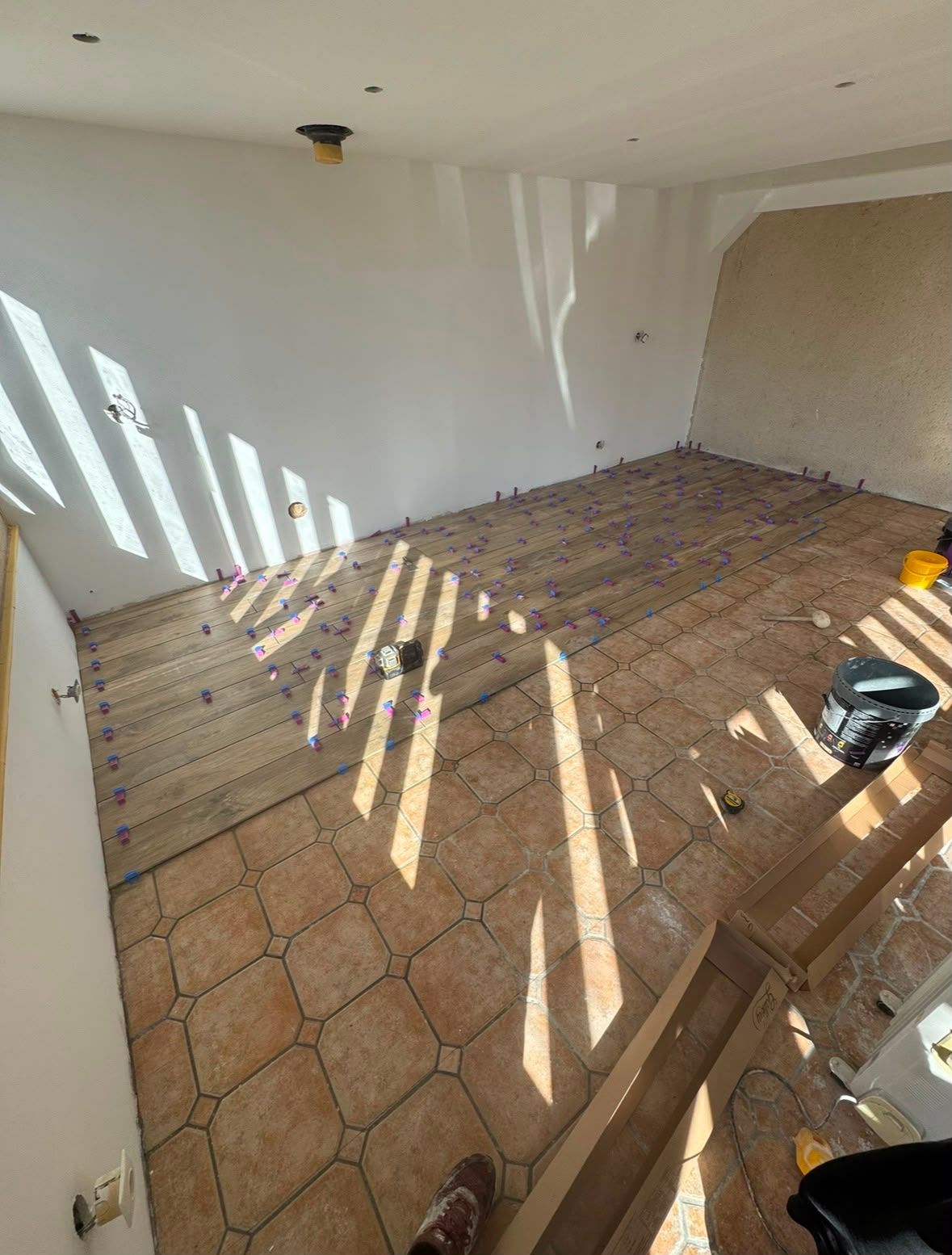 Pièce vide avec sol en terre cuite, murs blancs et lumière du soleil projetant des ombres rayées.