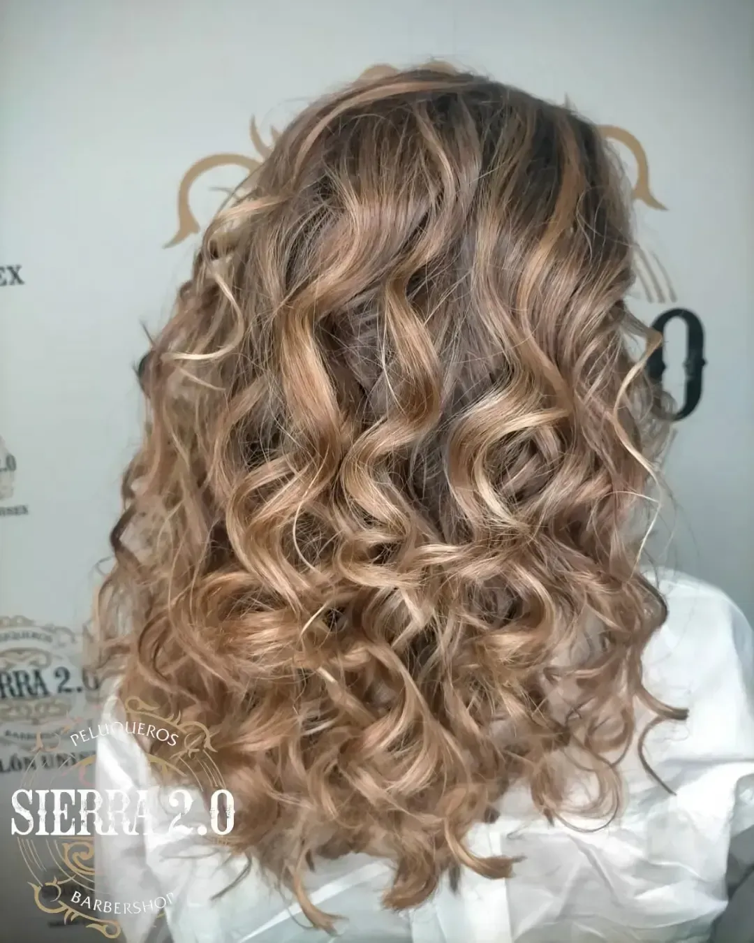 Vista posterior de una melena rubia rizada hasta los hombros con ondas sueltas.