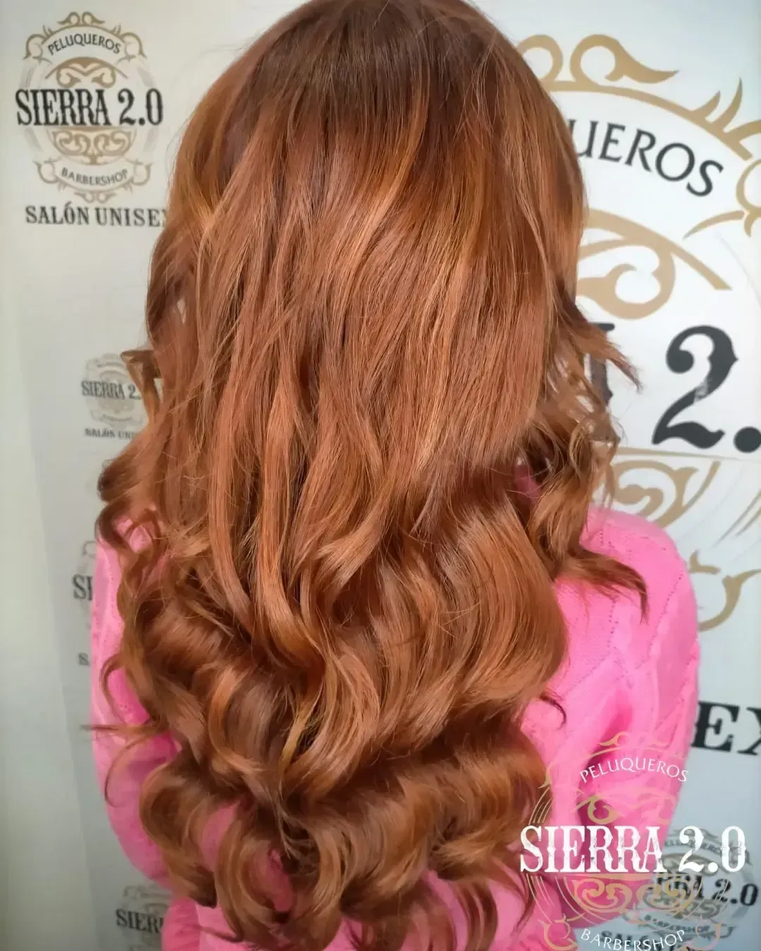 Cabello largo y ondulado color cobre peinado hacia abajo sobre un fondo de salón con logotipos.