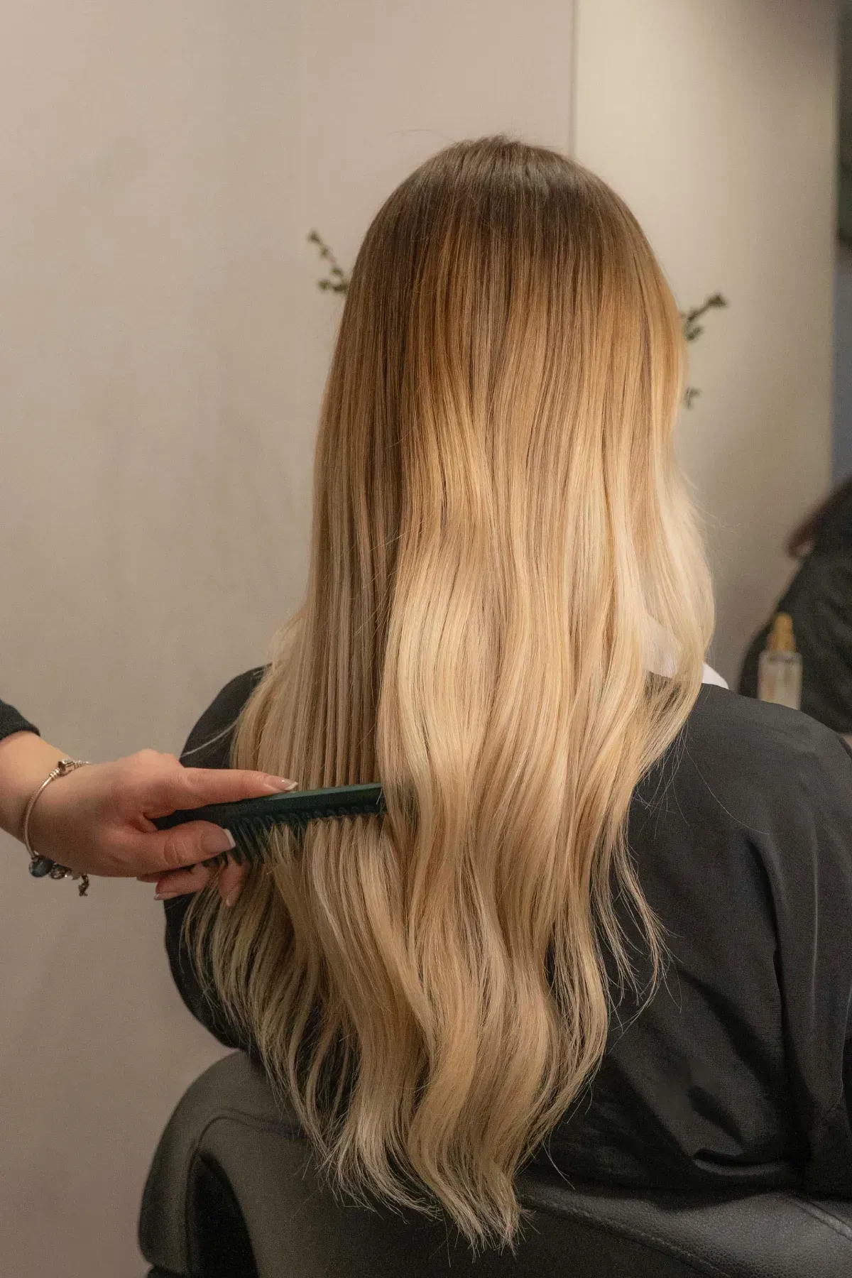 Cabello largo y ondulado castaño peinado hacia abajo contra un fondo de salón de belleza.