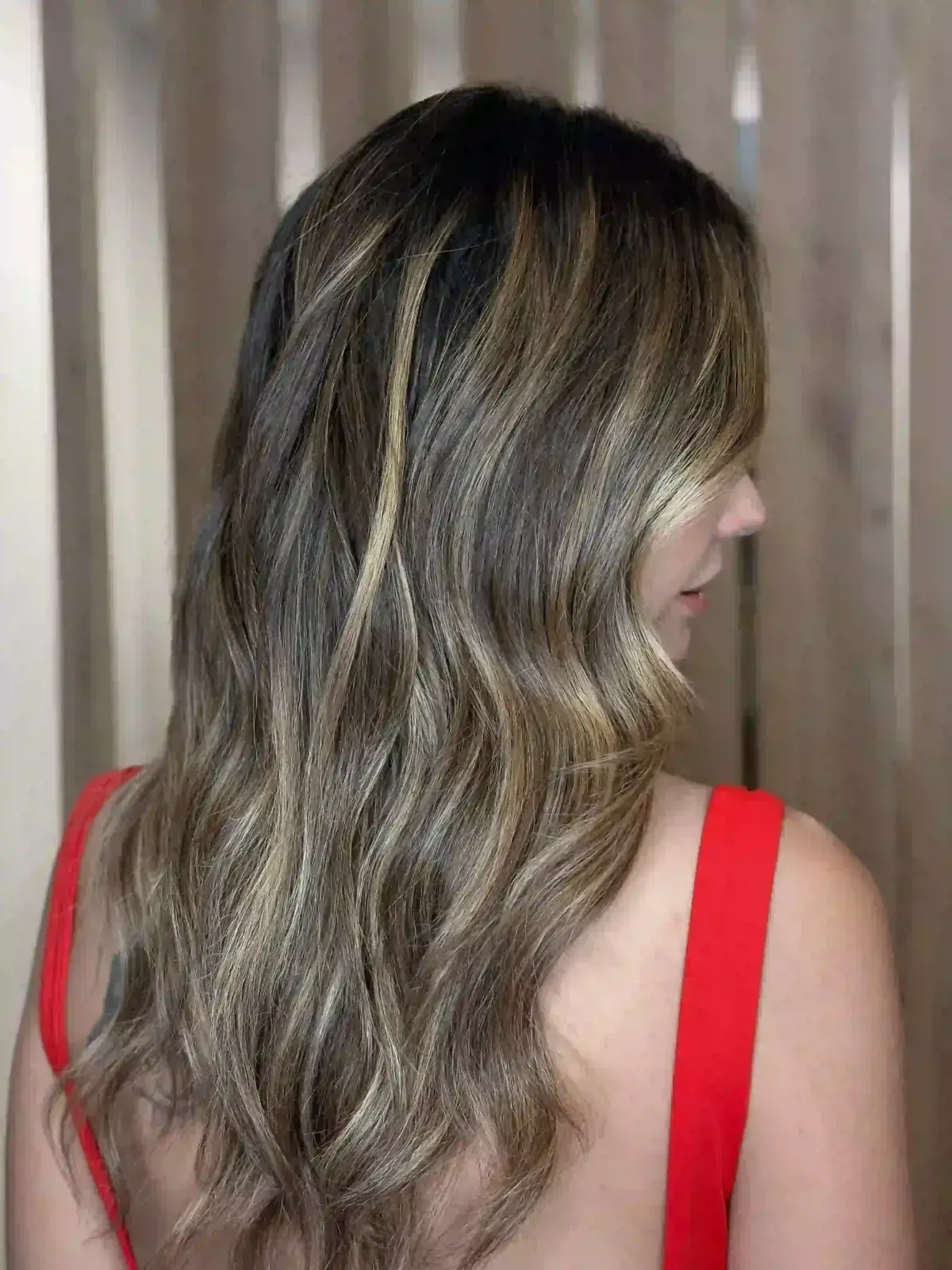 Mujer con cabello castaño ondulado y reflejos rubios, vista de espaldas con una blusa roja.