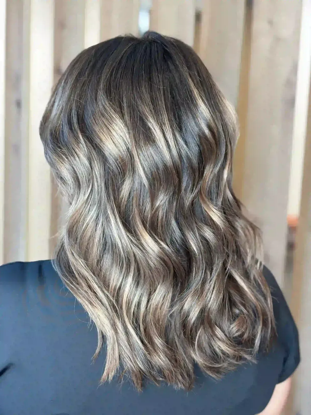 Cabello castaño ondulado hasta los hombros con reflejos rubios, que se ve desde atrás sobre una camisa oscura.