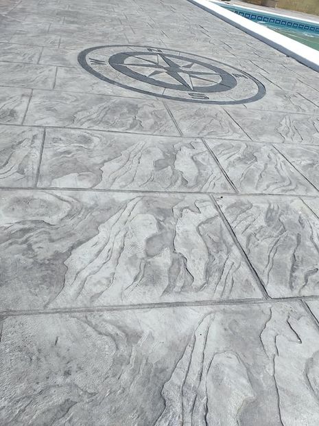Un suelo de hormigón con una brújula encima, al lado de una piscina.