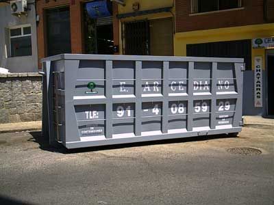 Un gran contenedor de basura gris está estacionado al costado de la carretera frente a un edificio.