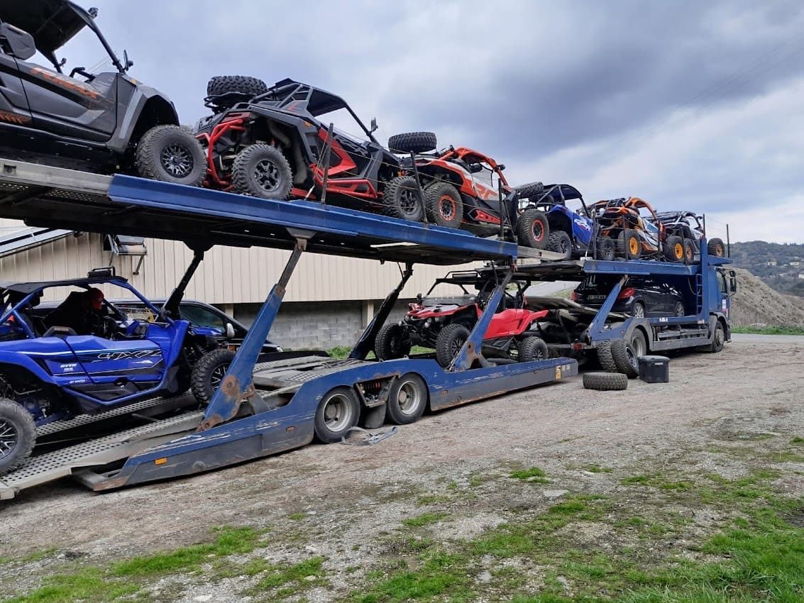 Un semirremolque transporta varios vehículos todoterreno de colores en un remolque, estacionado afuera.