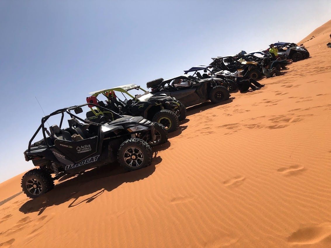 Vehículos todoterreno alineados sobre una duna de arena bajo un cielo brillante.