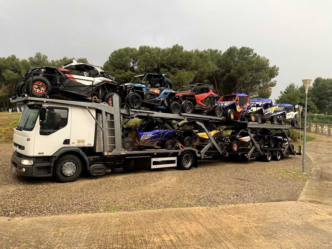 Un camión cargado con varios vehículos todoterreno, estacionado sobre una superficie de grava.
