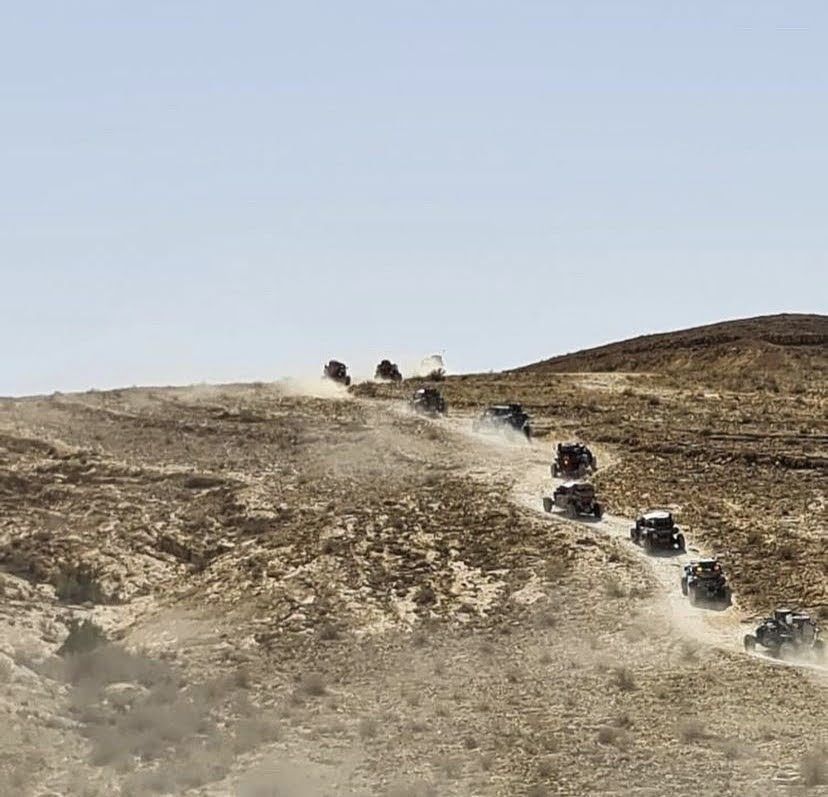 Vehículos todoterreno circulando por un sendero polvoriento cuesta arriba, en un paisaje desértico.