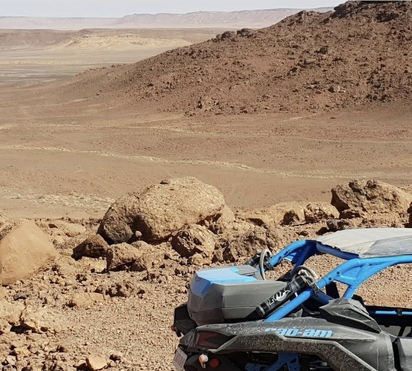 Vehículo todoterreno azul y negro en un paisaje desértico rocoso con colinas marrones al fondo.