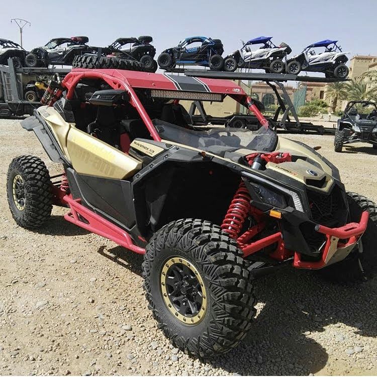 Vehículo todoterreno dorado y rojo con neumáticos grandes, estacionado al aire libre delante de otros vehículos.
