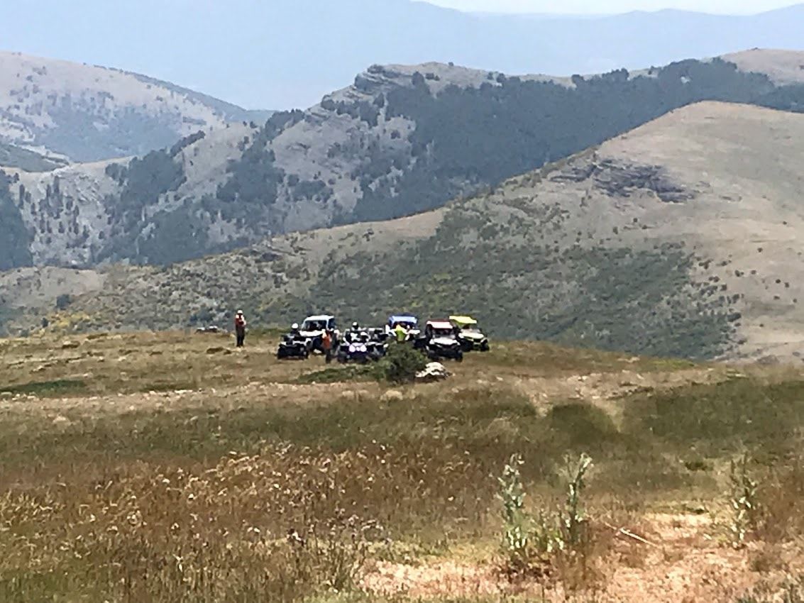 Varios vehículos todoterreno estacionados en la cima de una colina cubierta de hierba con vistas a las montañas.