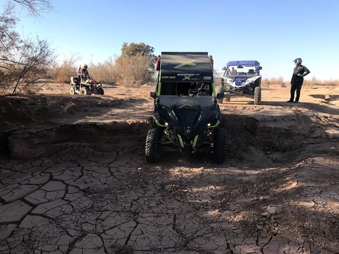 Vehículos todoterreno recorren un paisaje agrietado y seco; un UTV al frente, cuatrimotos y personas al fondo.