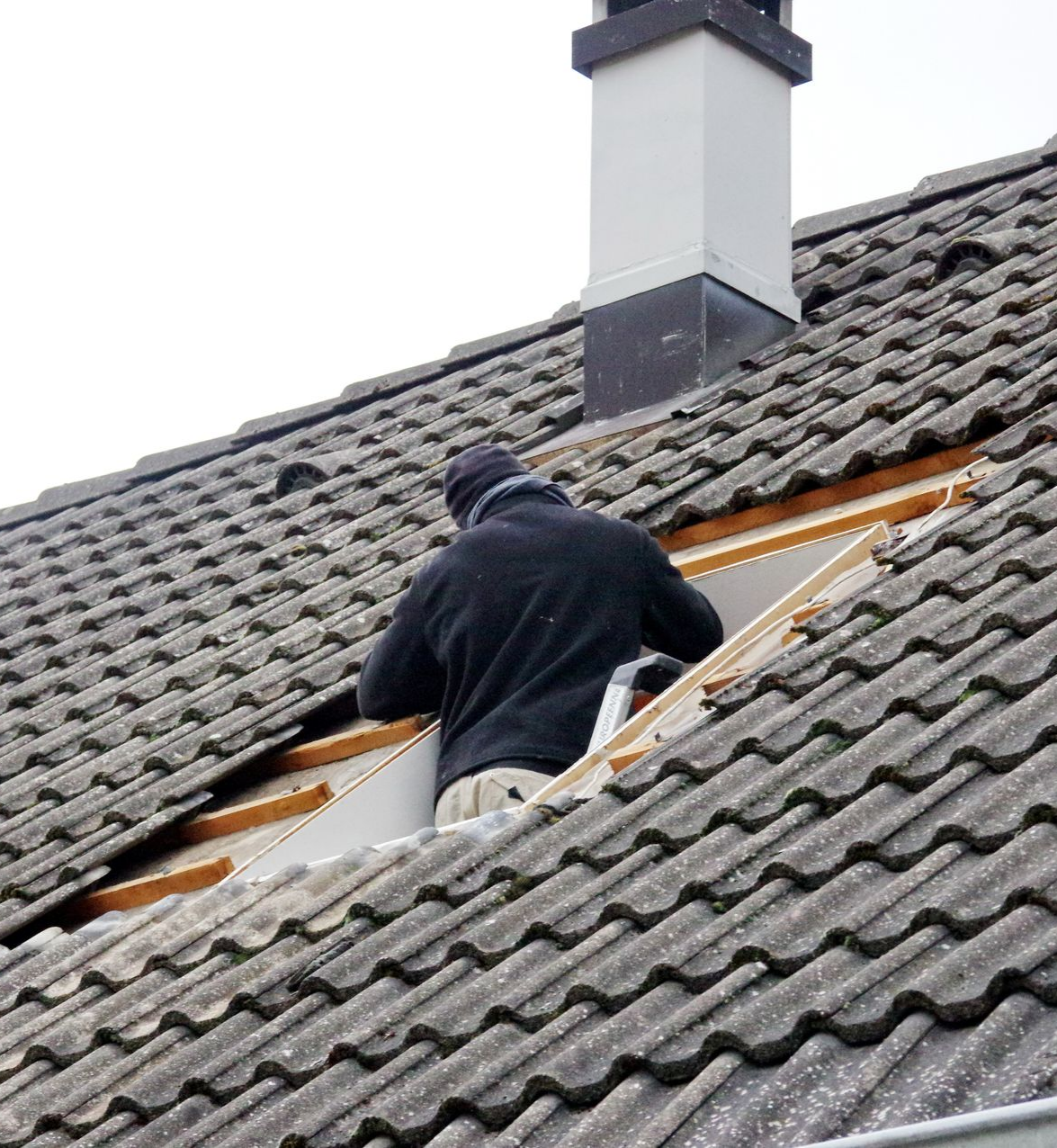 Une personne travaille sur un toit, près d'une cheminée.