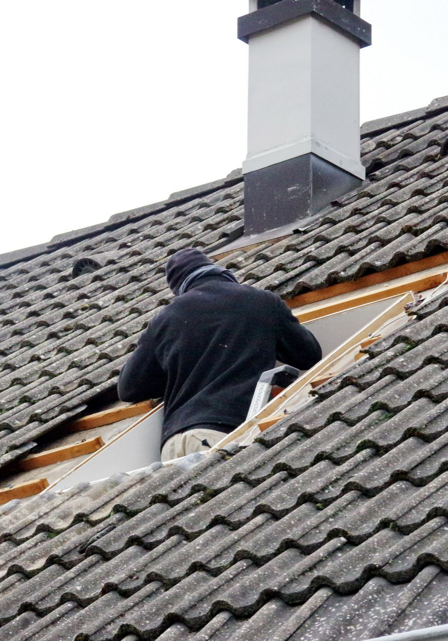 Une personne sur un toit répare une section près d'une cheminée.