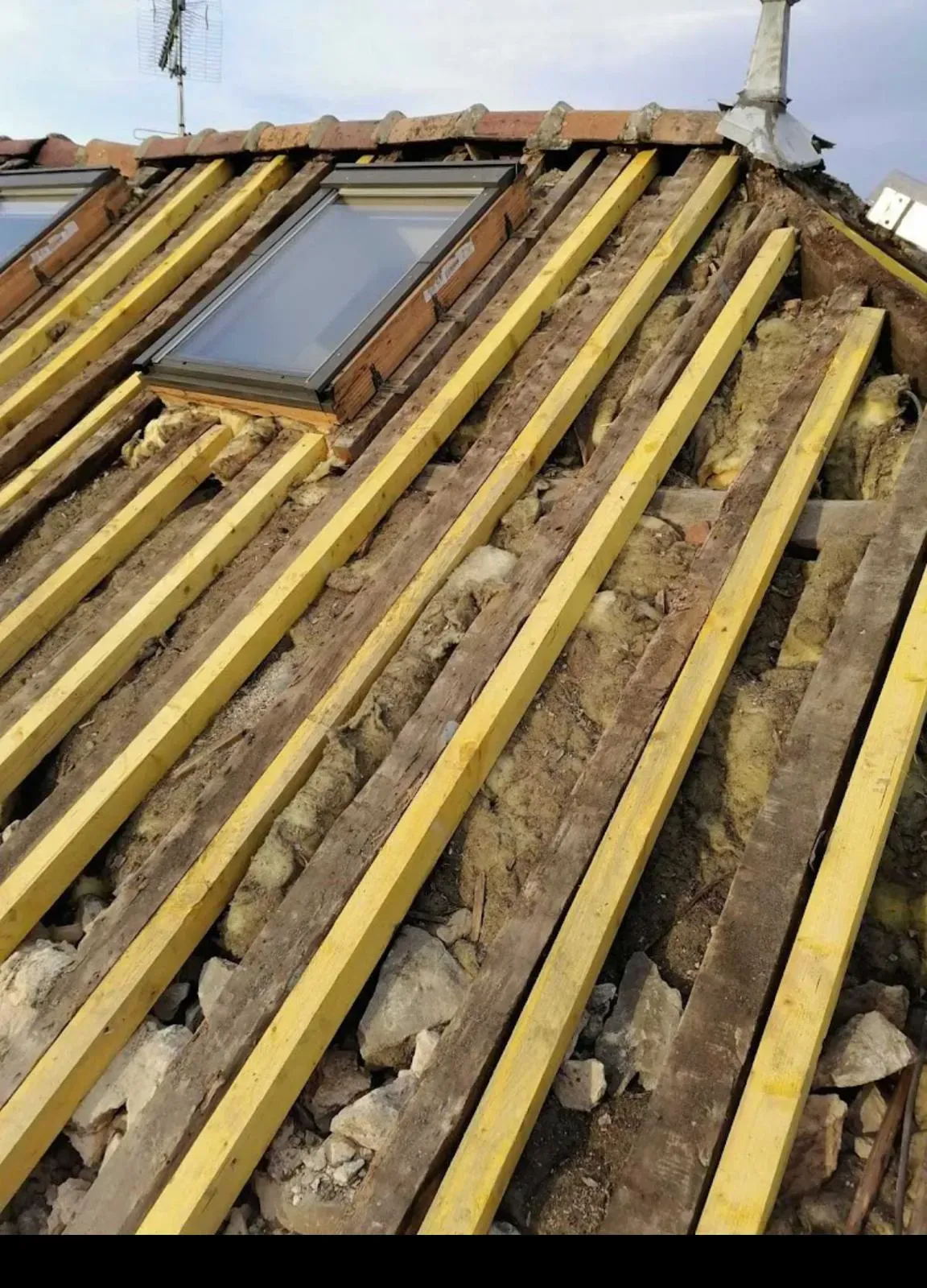 Toiture en cours de rénovation avec poutres apparentes, isolation et fenêtre de toit.