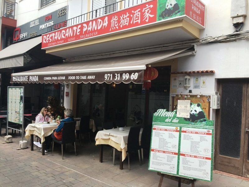 La gente está sentada en mesas afuera de un restaurante llamado Restaurante Panda.
