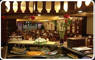 Un restaurante con muchas mesas y sillas y una mesa con un jarrón de flores encima.