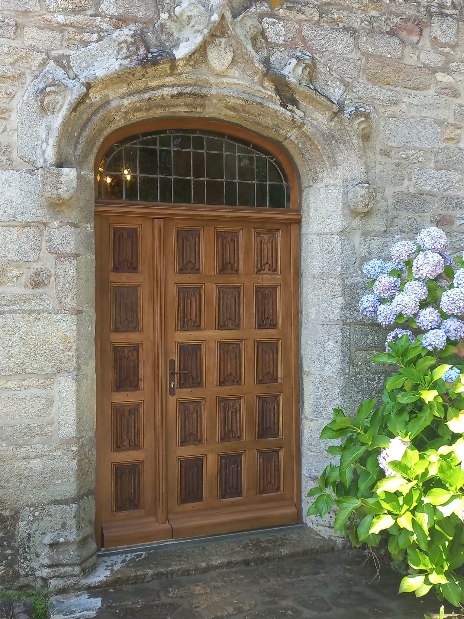 Porte cochère en bois dans un bâtiment en pierre avec un hortensia à côté