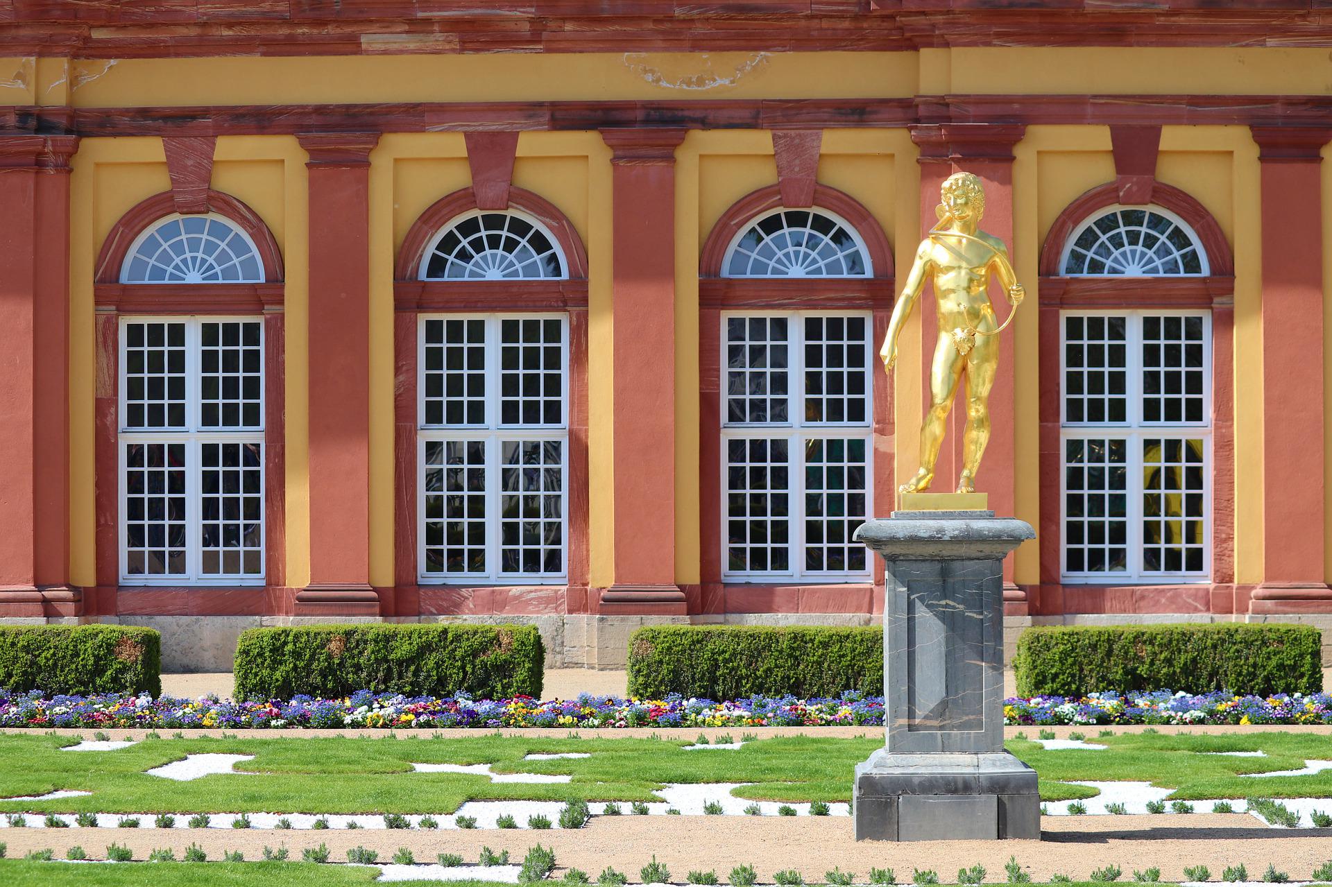 Statue dorée devant un bâtiment aux couleurs jaune safran et ocre rouge