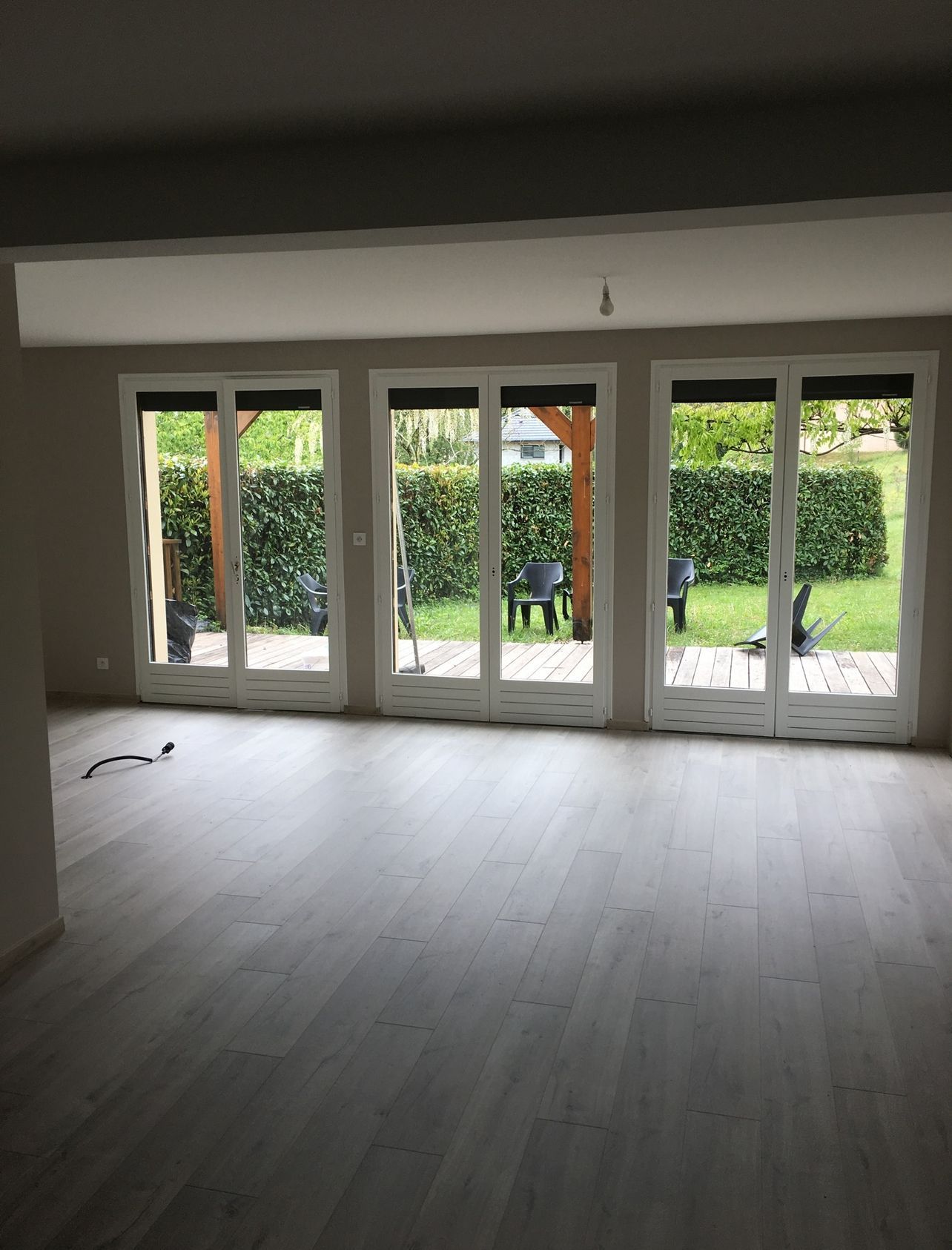 Photo d'un salon après la restauration du sol, des murs en plâtre et des baies vitrées.