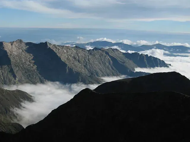 Una montaña cubierta de nubes con un cielo azul al fondo.