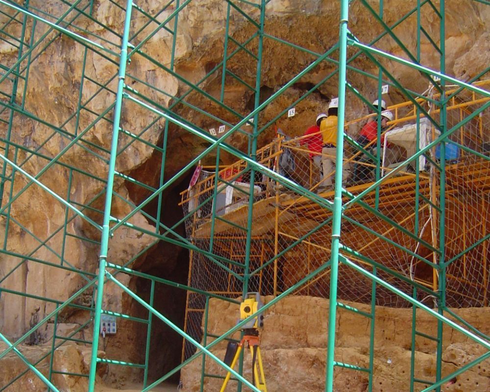 Un grupo de personas de pie sobre un andamio frente a una cueva.