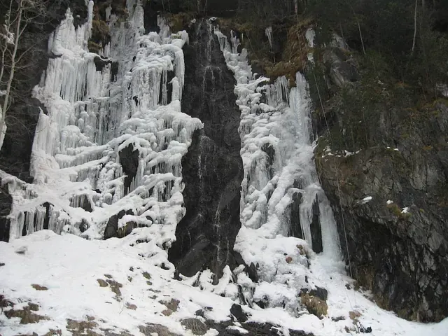 Una cascada congelada está rodeada de nieve y rocas.