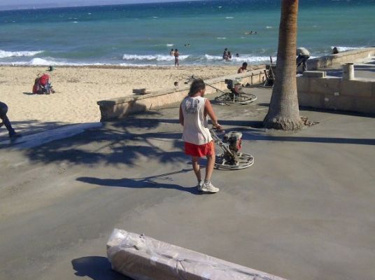 Un hombre empujando un cochecito en una acera cerca de la playa.