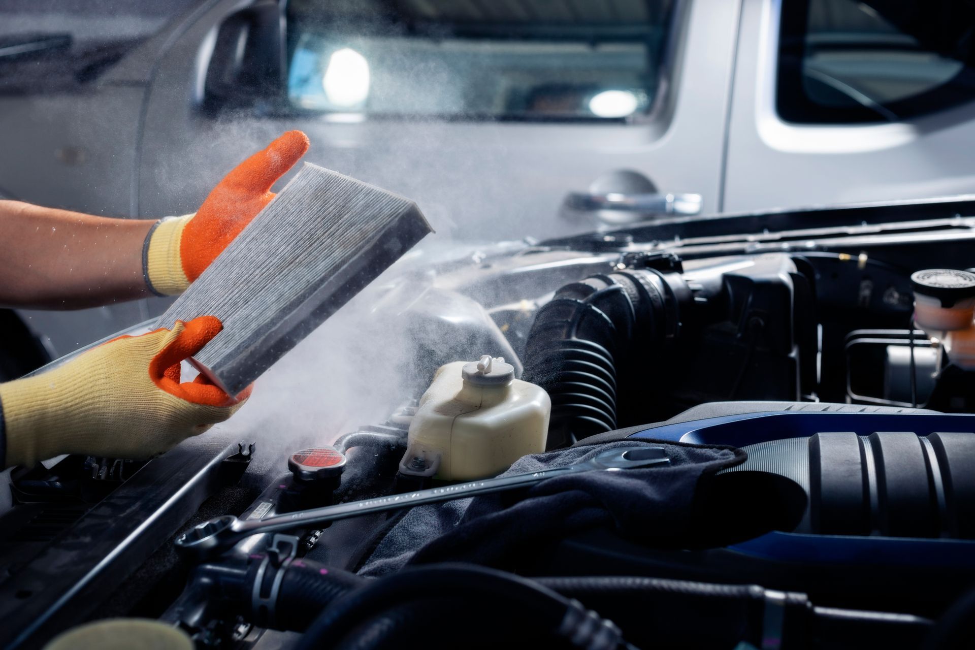 Un mécanicien avec un filtre à air dans les mains, devant une voiture.
