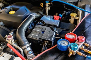 Compartiment moteur de voiture avec prise d'air, batterie et manomètres de niveau de réfrigérant colorés reliés à des tuyaux.
