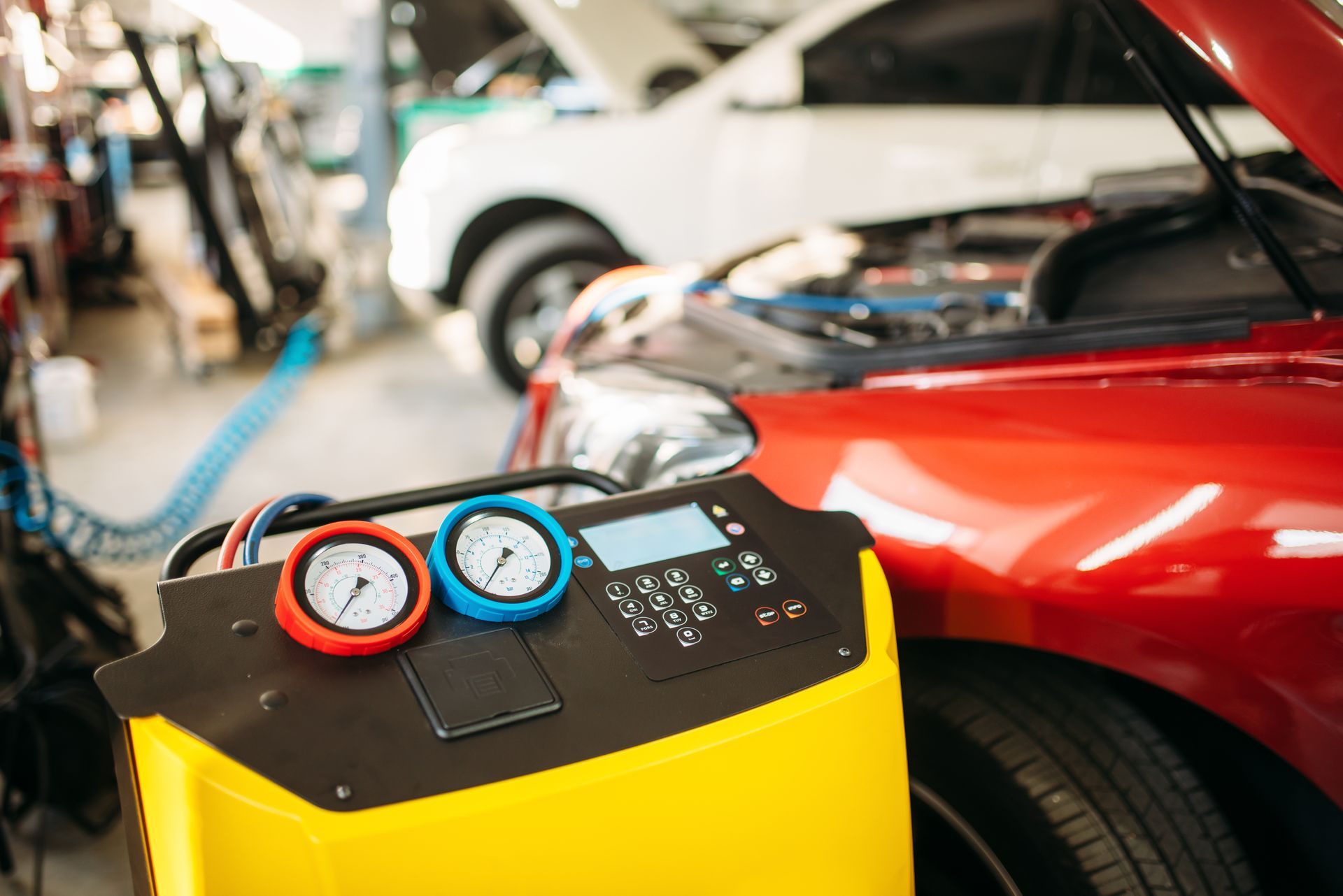 Manomètres et machine de contrôle de la climatisation automobile à côté d'une voiture rouge dans un garage.