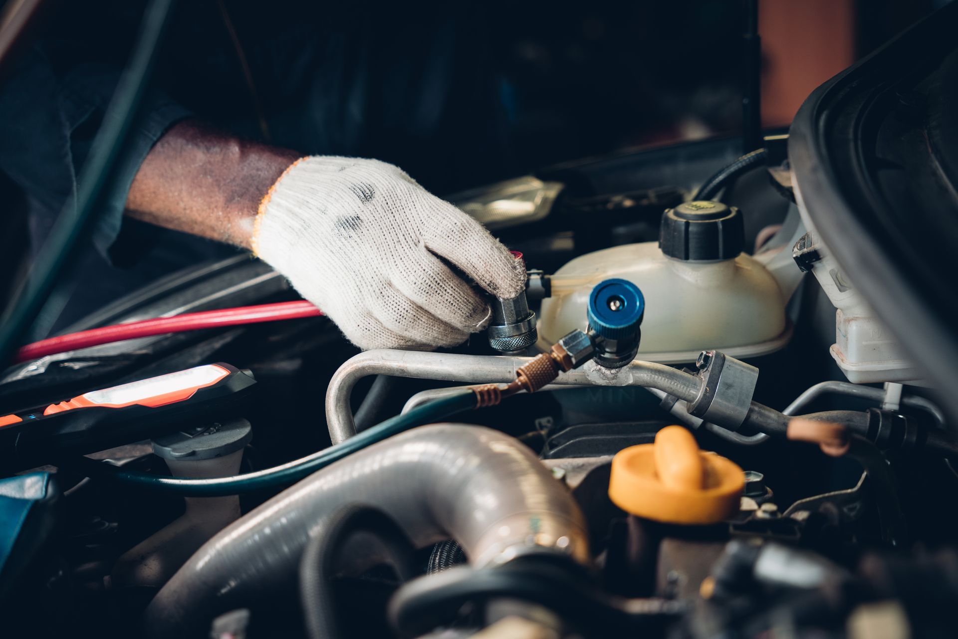 Un mécanicien ganté travaille sous le capot d'une voiture, ajustant les composants du moteur à l'aide d'outils.