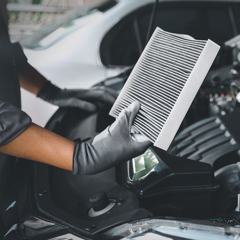 Des mains gantées tiennent un filtre à air de moteur de voiture au-dessus d'un capot ouvert