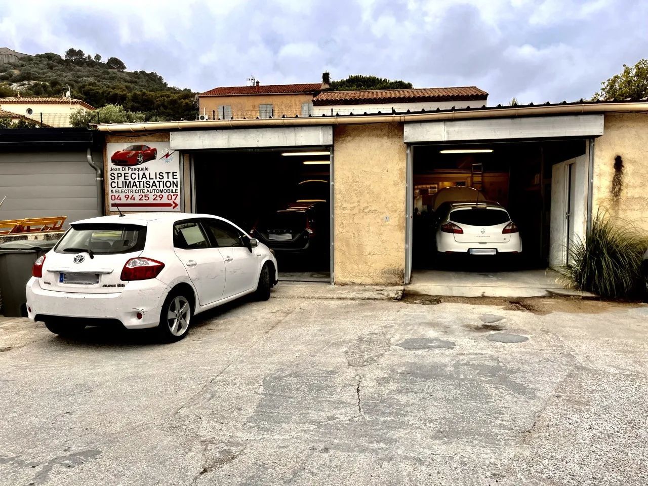 Deux voitures blanches garées devant un petit garage aux emplacements ouverts par temps nuageux