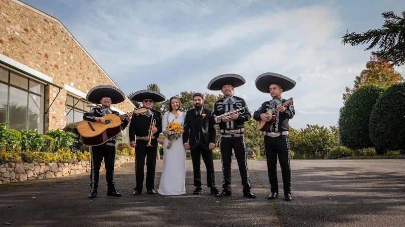Pareja de novios con mariachis. Músicos vestidos de negro, tocando instrumentos al aire libre.