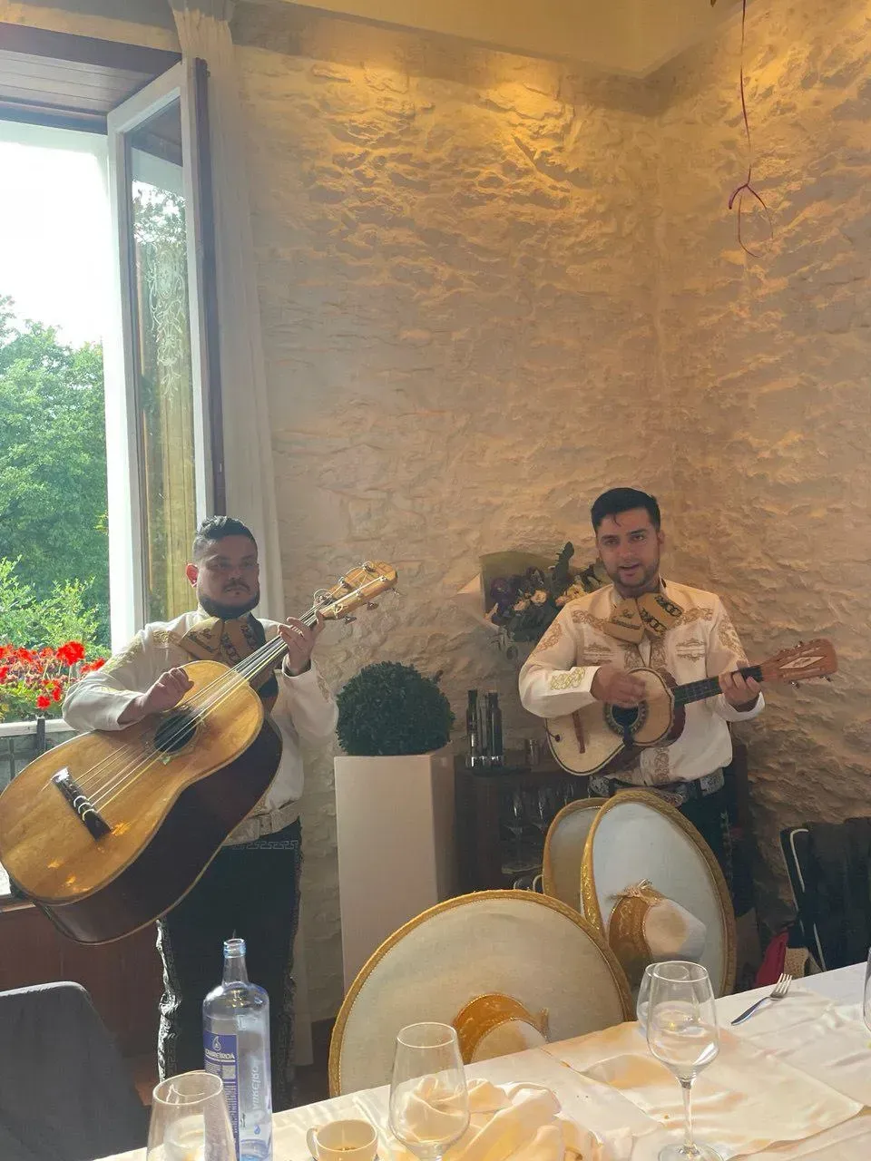 Dos músicos de mariachi tocando instrumentos en una mesa de un restaurante.