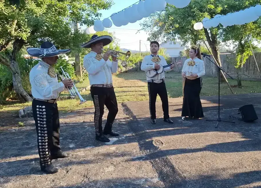 Mariachis tocando al aire libre, con atuendos tradicionales. Dos trompetistas, un guitarrista y un vocalista.