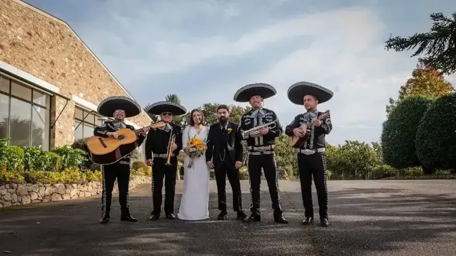 Mariachi con novios posando al aire libre. Los músicos visten trajes tradicionales y sostienen instrumentos.