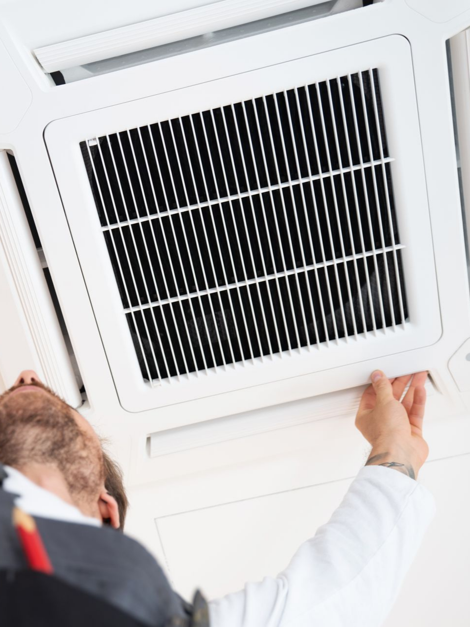 Une personne inspecte une grille d'aération blanche fixée au plafond.