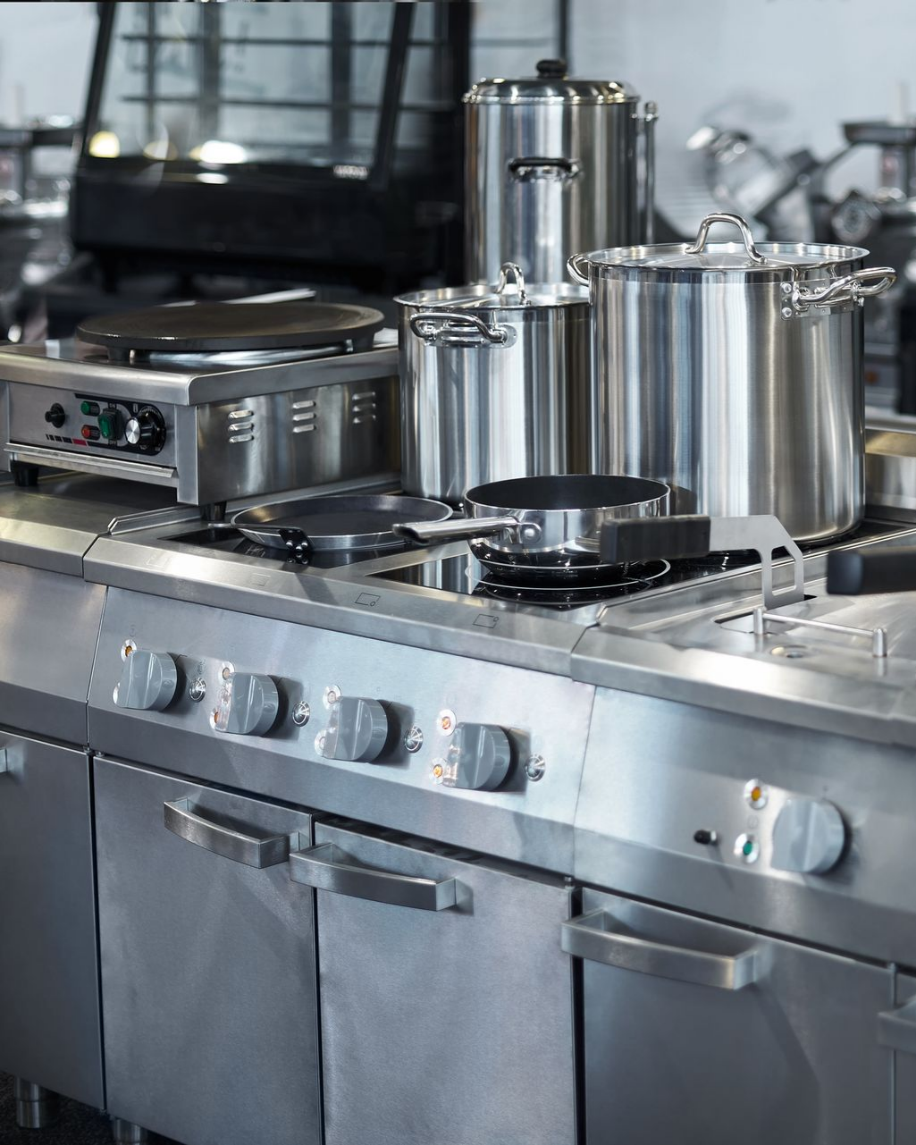 Gamme de cuisines professionnelles en acier inoxydable avec casseroles, poêles et appareils électroménagers.