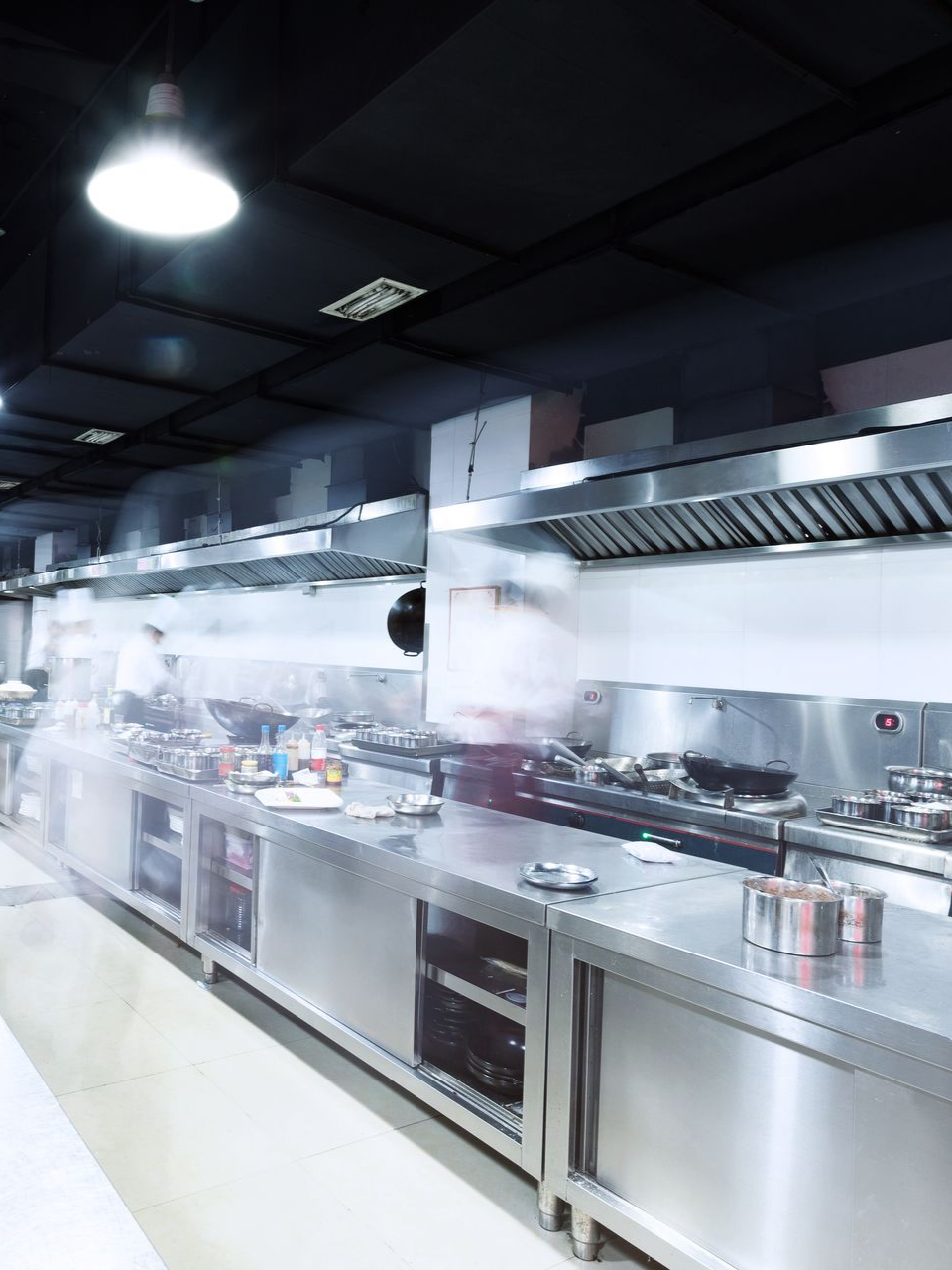 Cuisine professionnelle avec comptoirs et appareils en acier inoxydable, vapeur s'échappant.