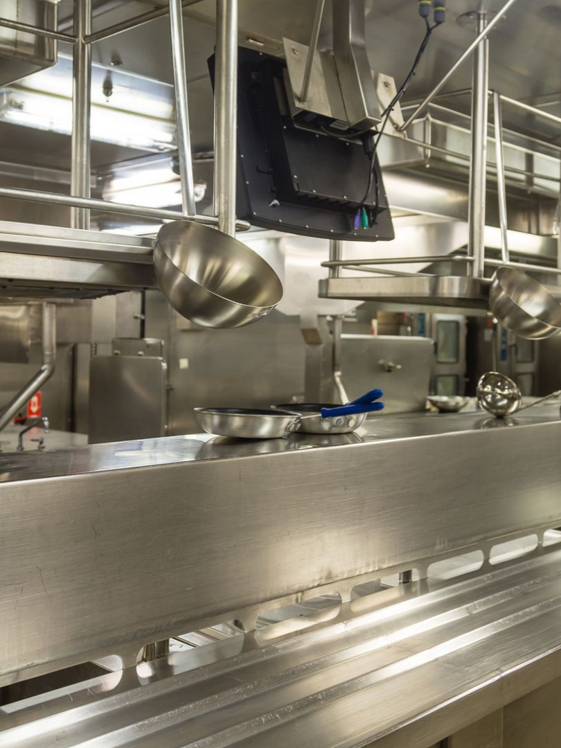 Cuisine commerciale en acier inoxydable avec casseroles, ustensiles et système de ventilation.