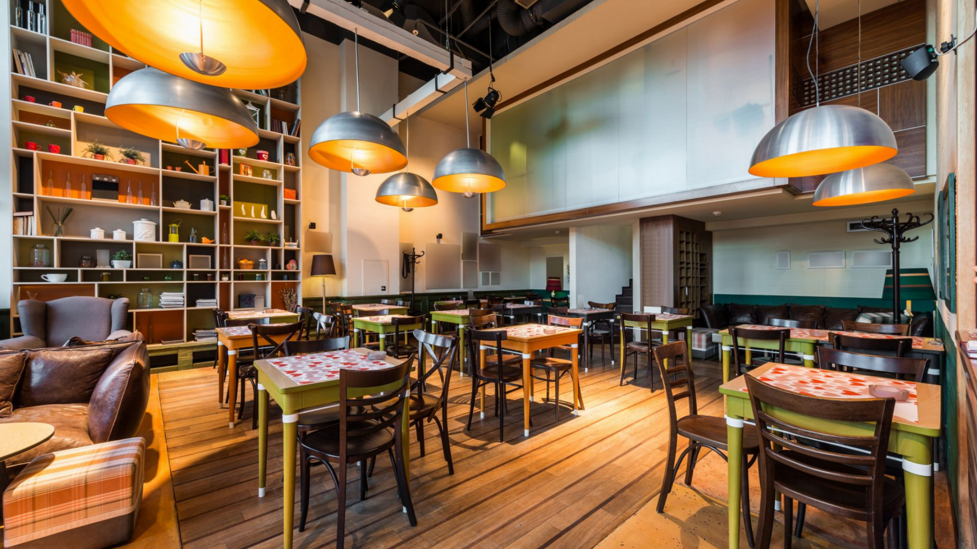 Intérieur de restaurant avec tables et chaises, grandes étagères et lampes suspendues.