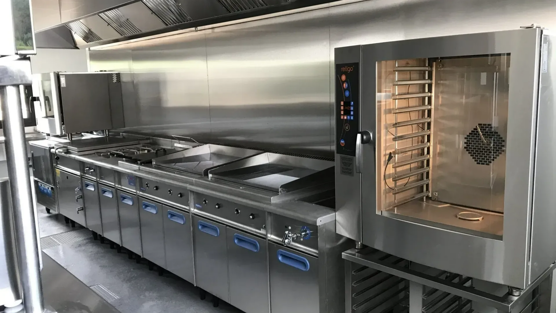Cuisine professionnelle équipée d'appareils en acier inoxydable : four, cuisinière et hotte.